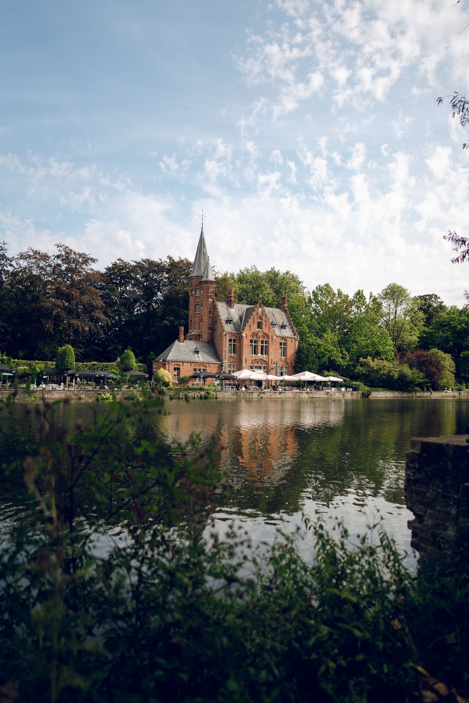 Picturesque church with spire reflected in calm lake waters surrounded by trees.