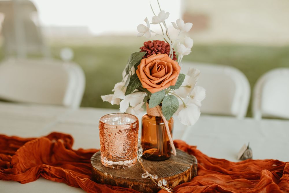 Wedding table decor featuring orange roses and candles on white linens.