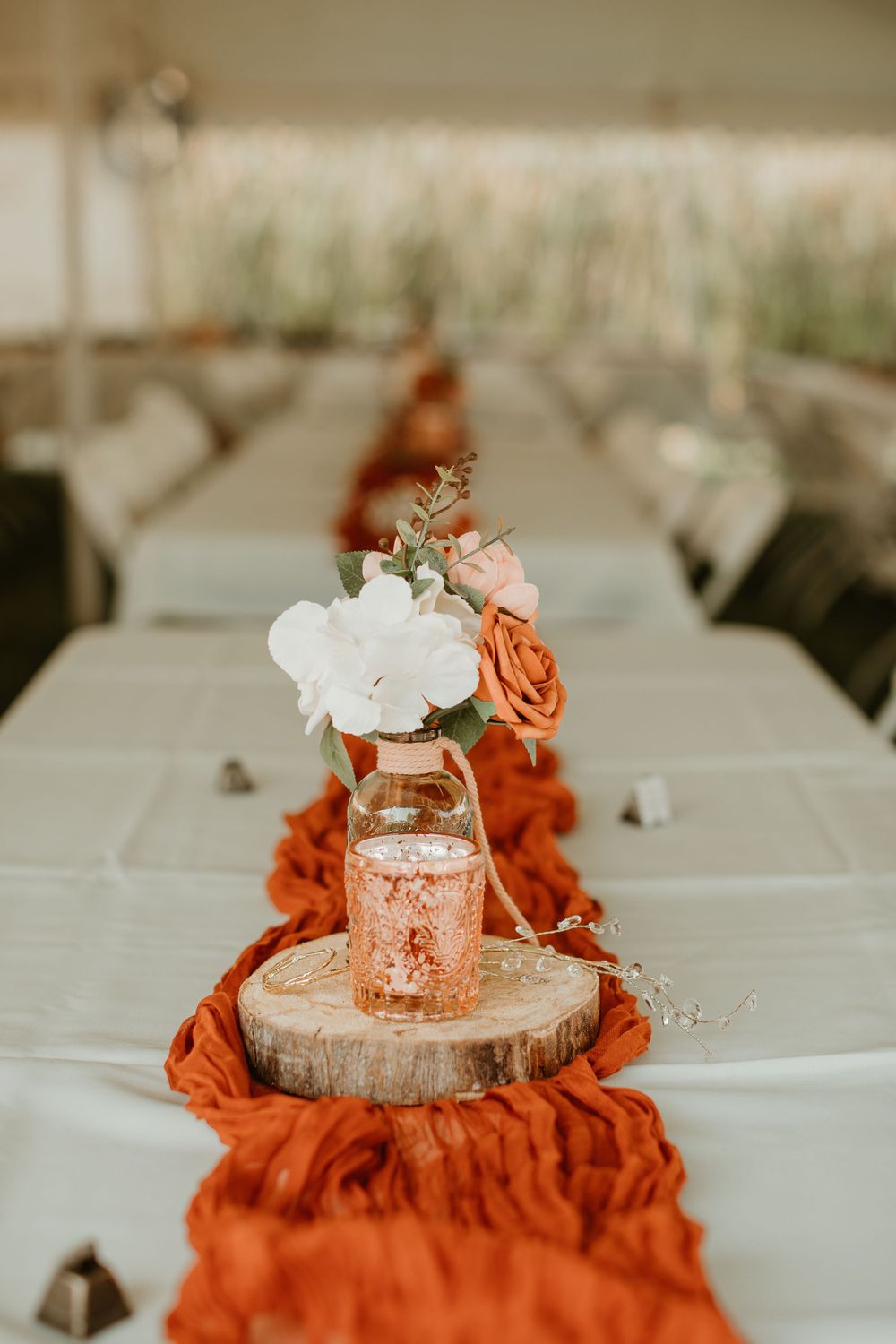 Rustic centerpieces with wood slices, orange fabric, and glowing votives on white tablecloths.