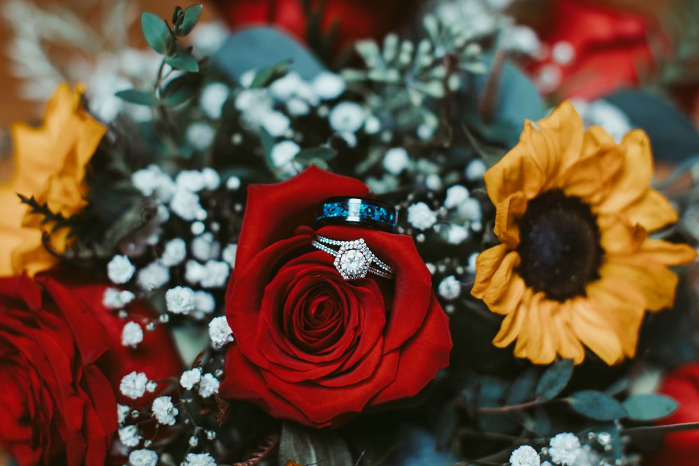 Wedding bouquet featuring red roses, sunflowers, and baby's breath with greenery accents.