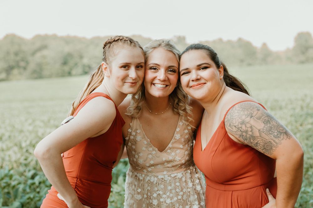 Wedding party members in coordinating orange and neutral dresses pose together outdoors.