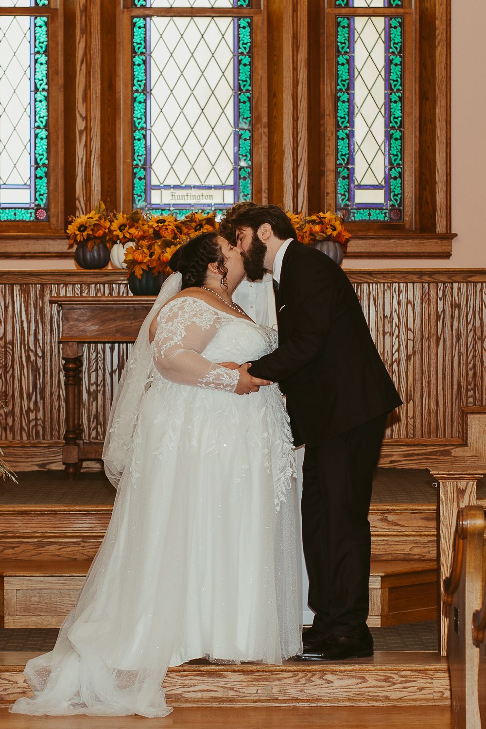 Wedding ceremony in progress inside historic church with stained glass windows and wooden details.