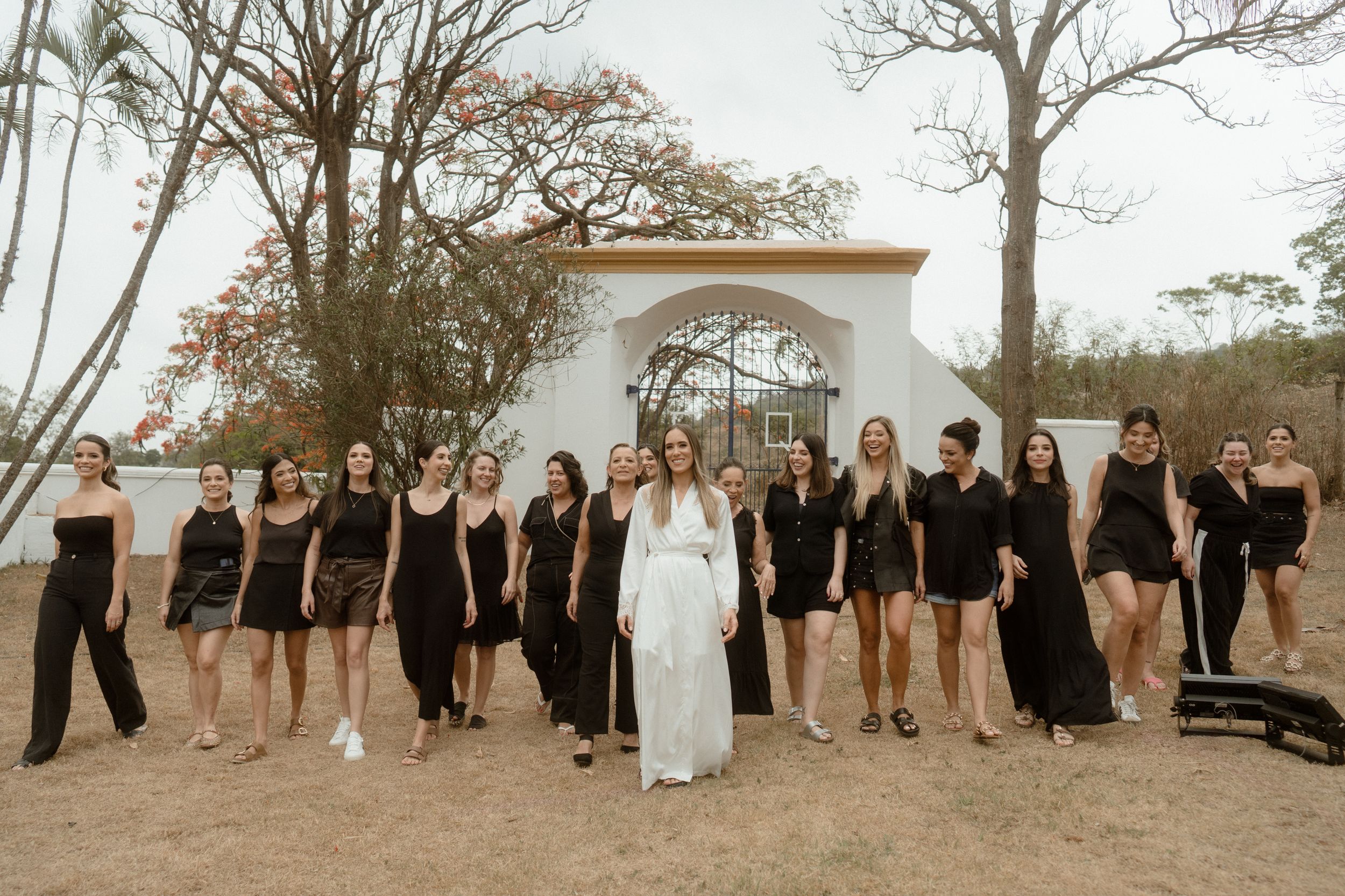 Wedding party group photo arranged on a lawn with autumn trees in the background.
