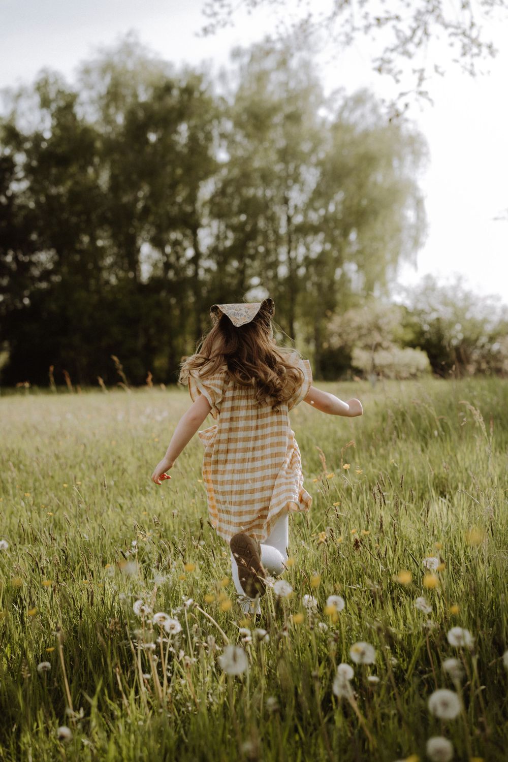 Person in gingham dress running through field of dandelions at golden hour.