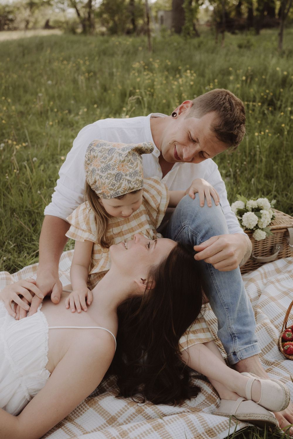 Family relaxing on picnic blanket in sunny meadow.