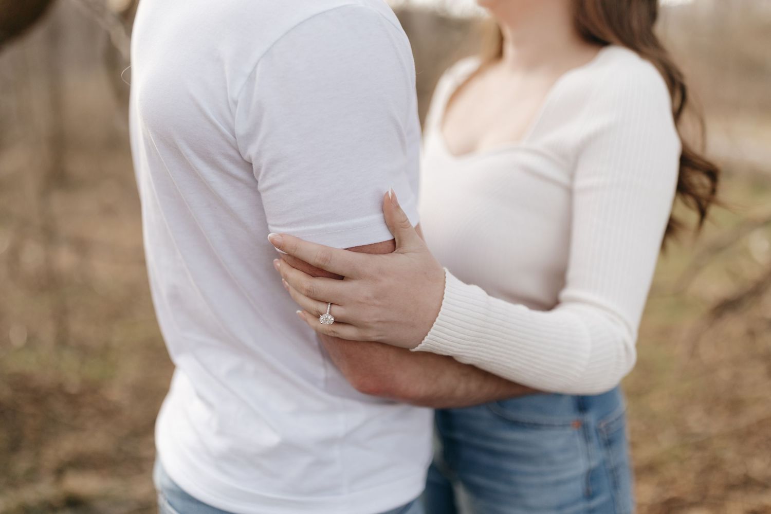 Close-up shot of a couple embracing in white tops and jeans during an outdoor photoshoot.
