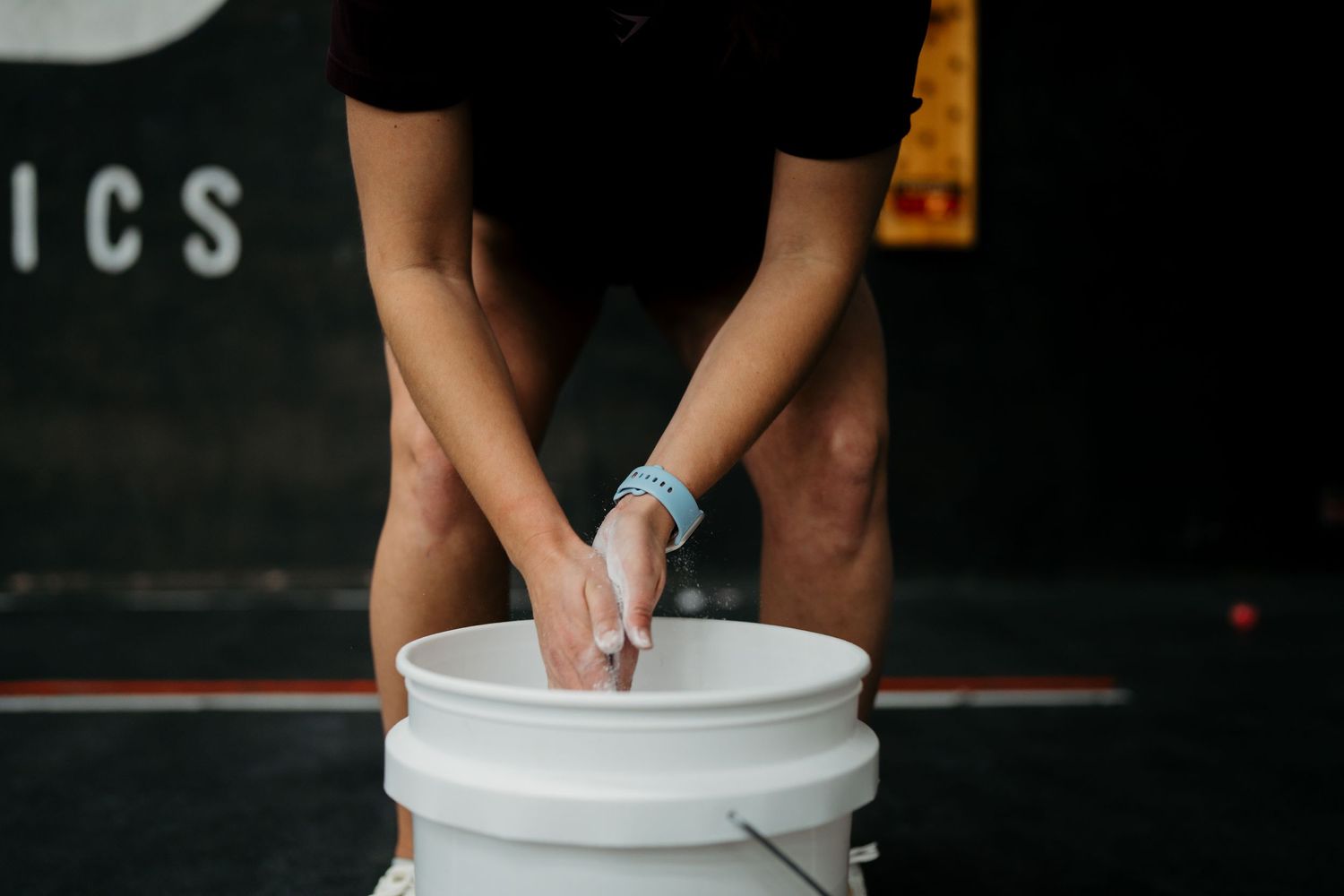 Athletic preparation showing hands applying chalk over a white bucket in dim lighting.