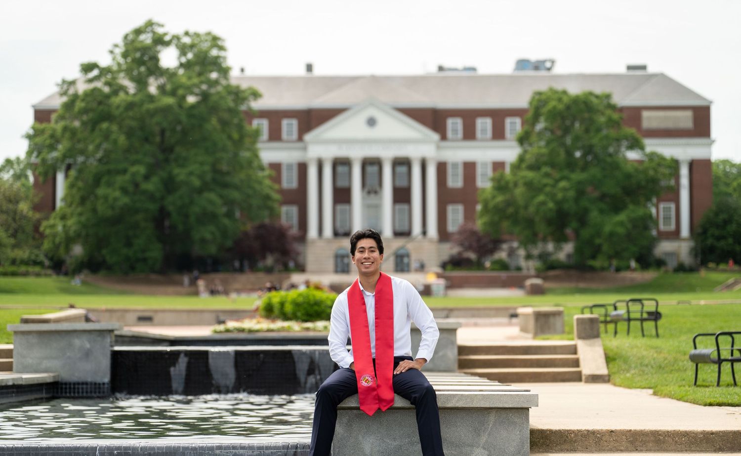 Graduate posing in front of stately white columned building with reflecting pool.