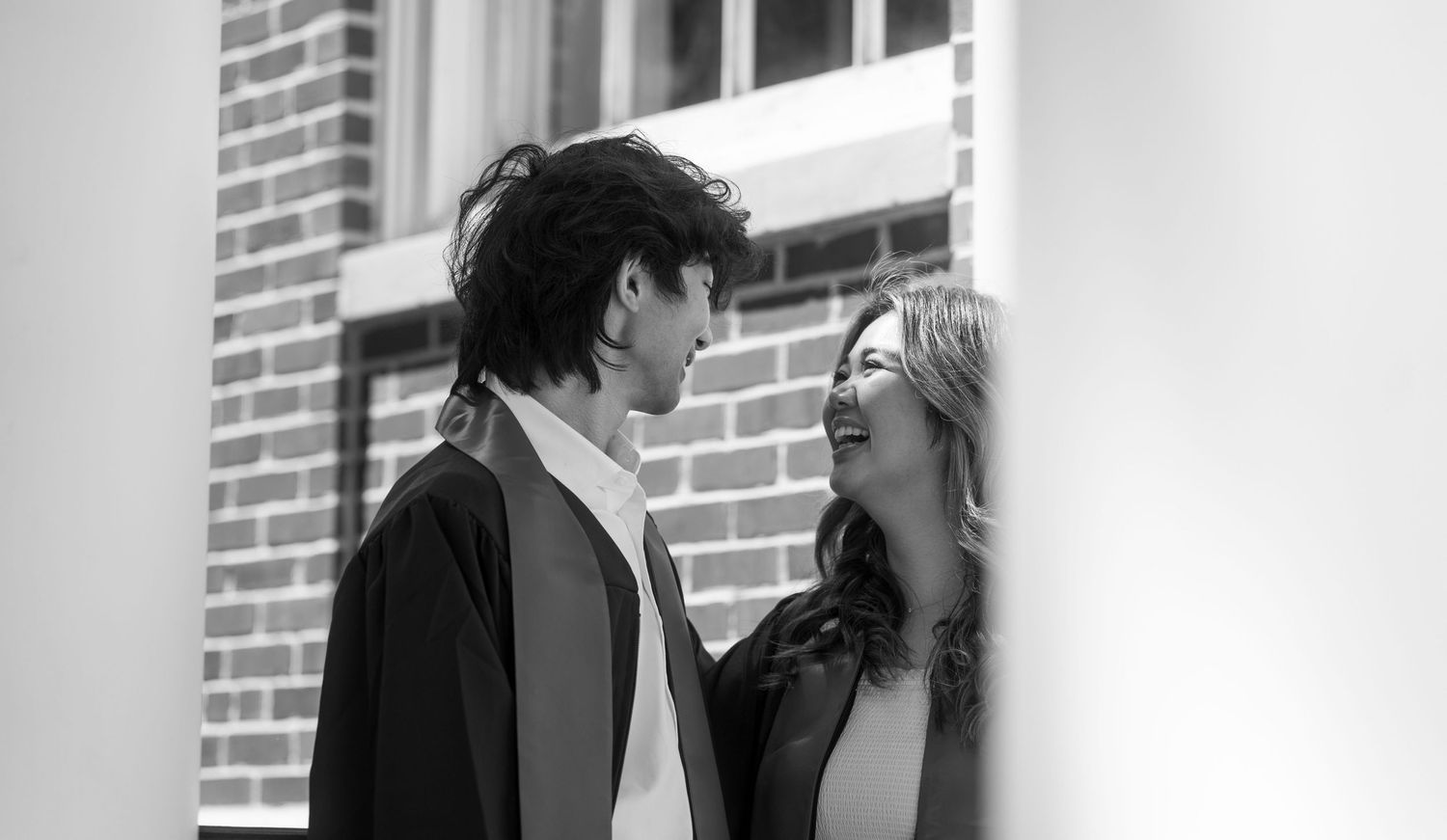 Black and white portrait of graduates sharing a moment near brick wall.