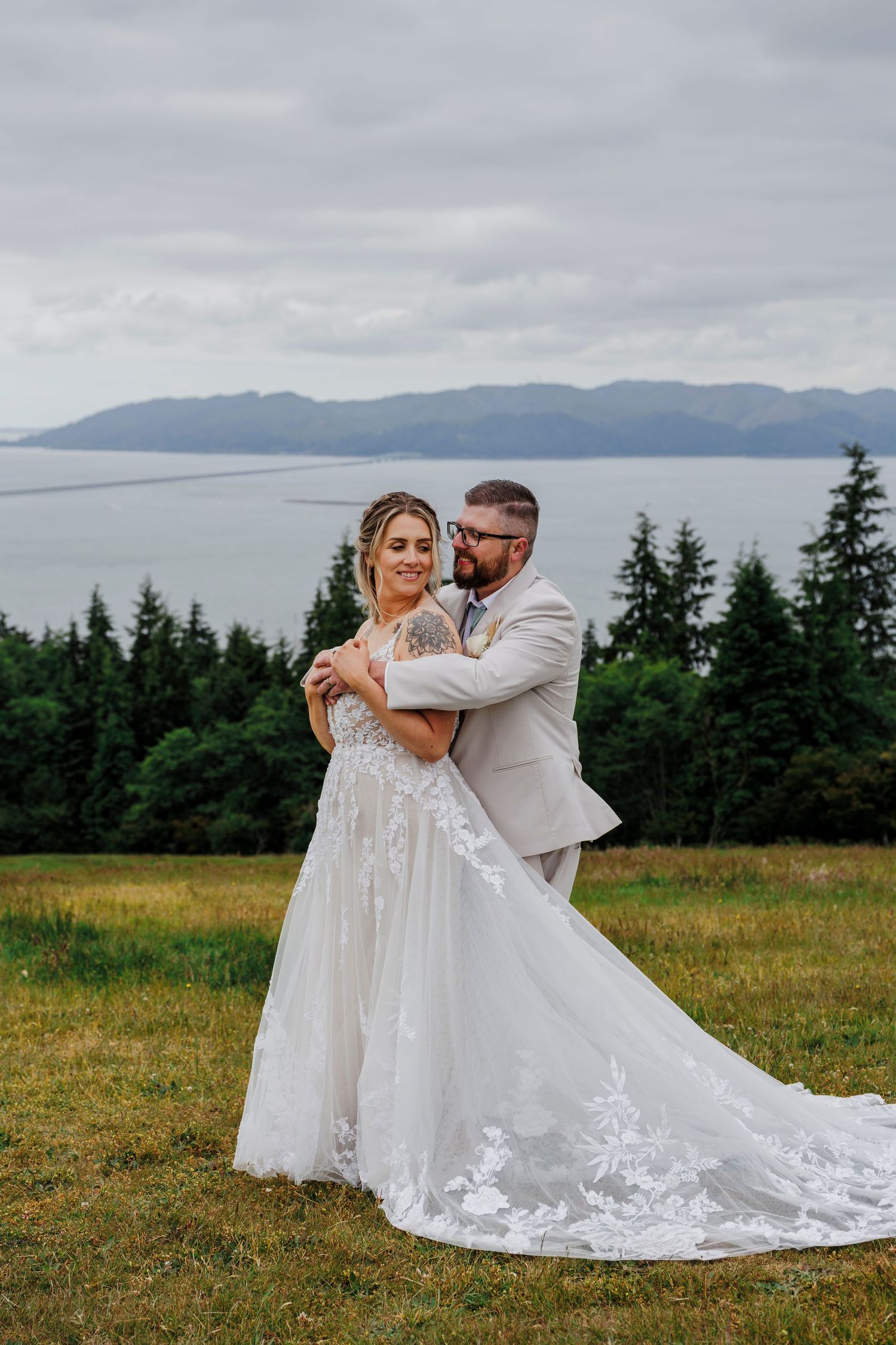 A couple shares an intimate embrace in a scenic mountain meadow with a white wedding dress flowing in the summer breeze.