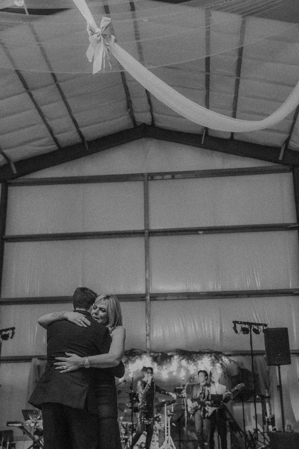 A black and white photograph of couple dancing together at an indoor venue with band equipment in the background.