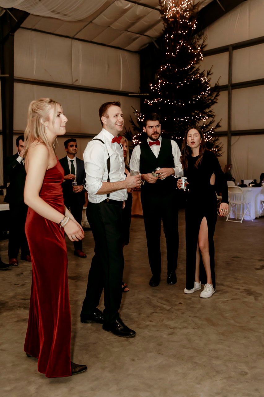 People gather for a holiday celebration at an indoor venue with a decorated Christmas tree and elegant formal attire.