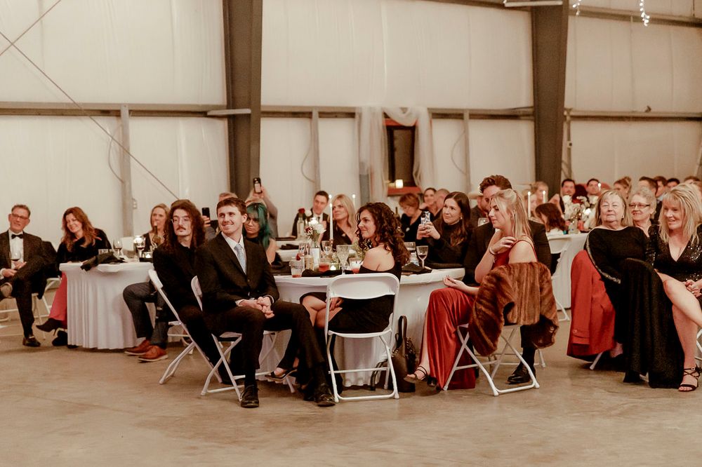 A group of people in formal attire seated at round tables during an indoor event in a warehouse-style venue.
