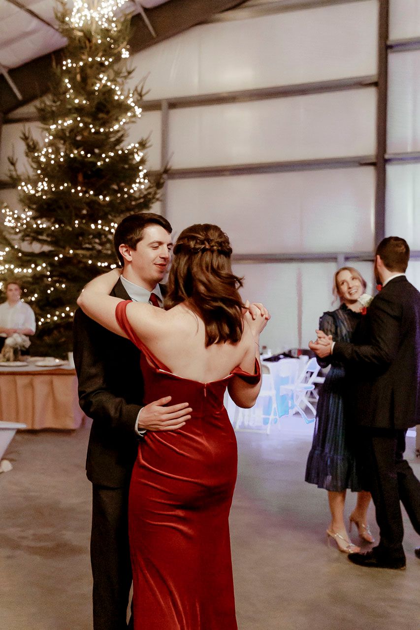 A couple dances at a holiday party with a decorated Christmas tree in the background.