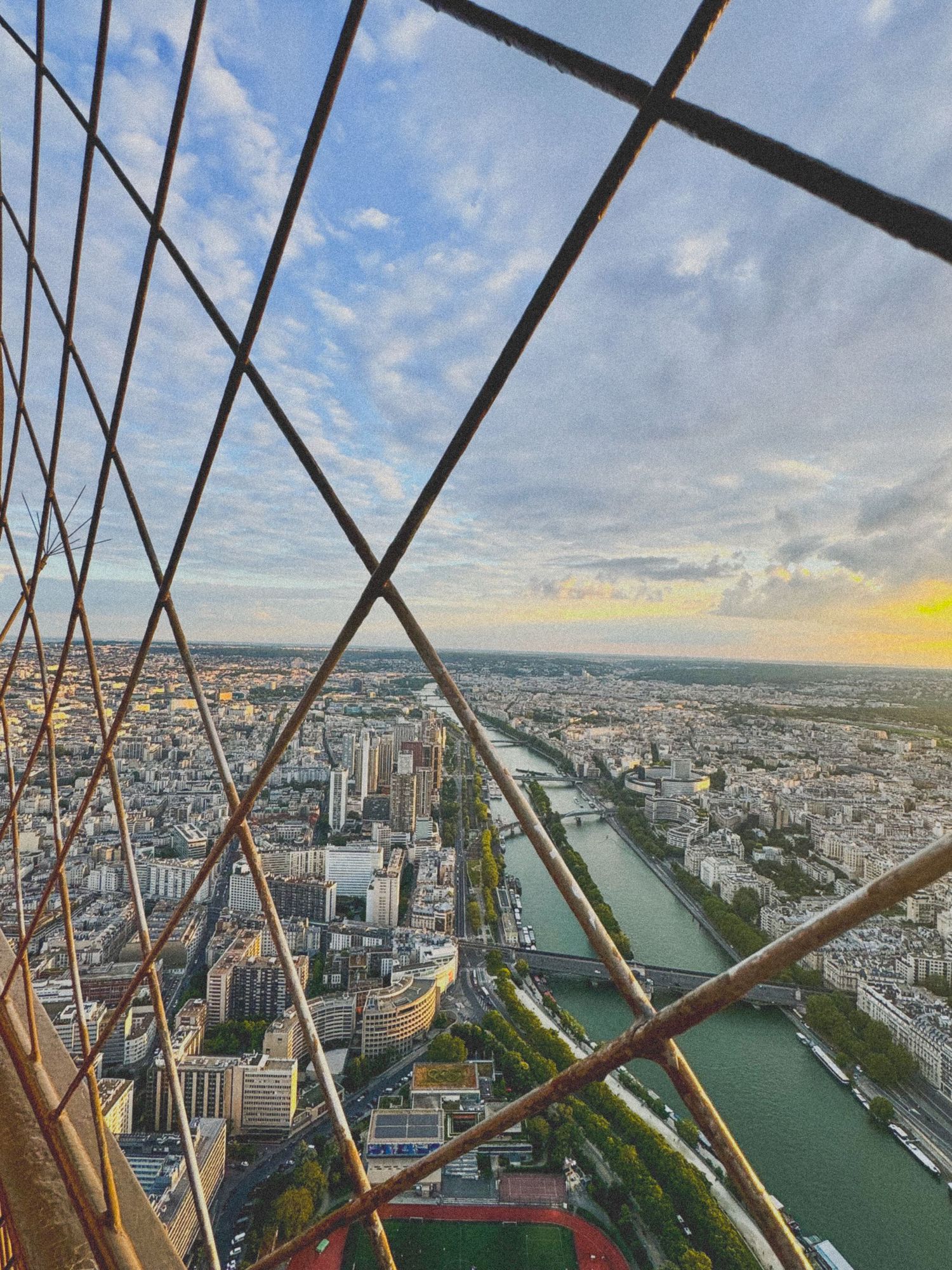 Scenic Paris cityscape viewed through Eiffel Tower's iron lattice during golden hour.