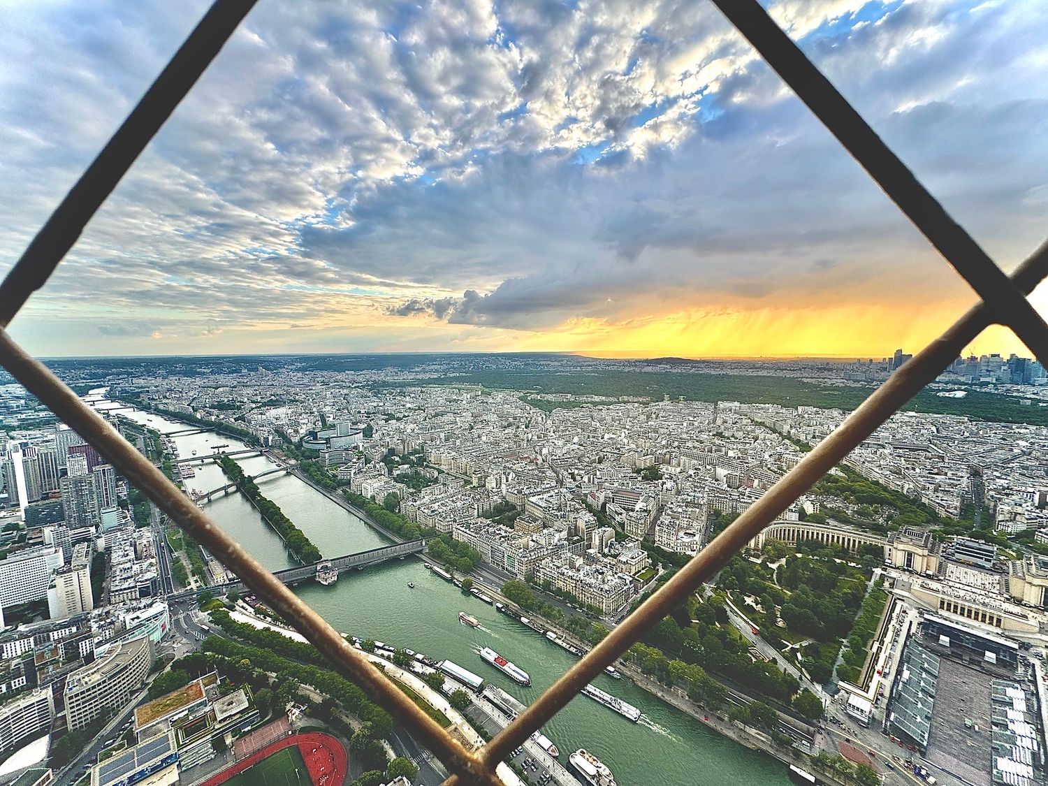 Aerial view of Paris cityscape and Seine River through Eiffel Tower framework at sunset.