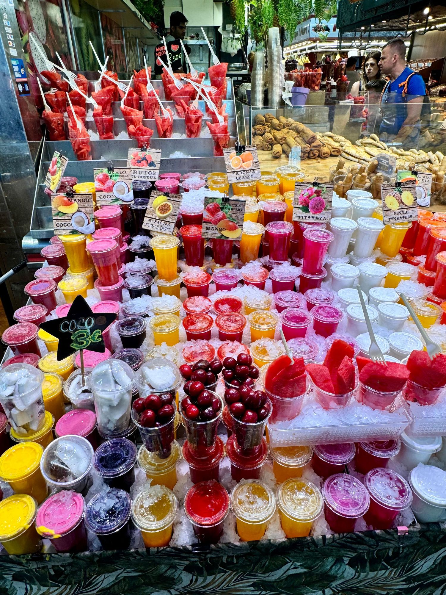 Colorful array of fresh fruit juices and smoothies displayed in plastic cups at a market stall.