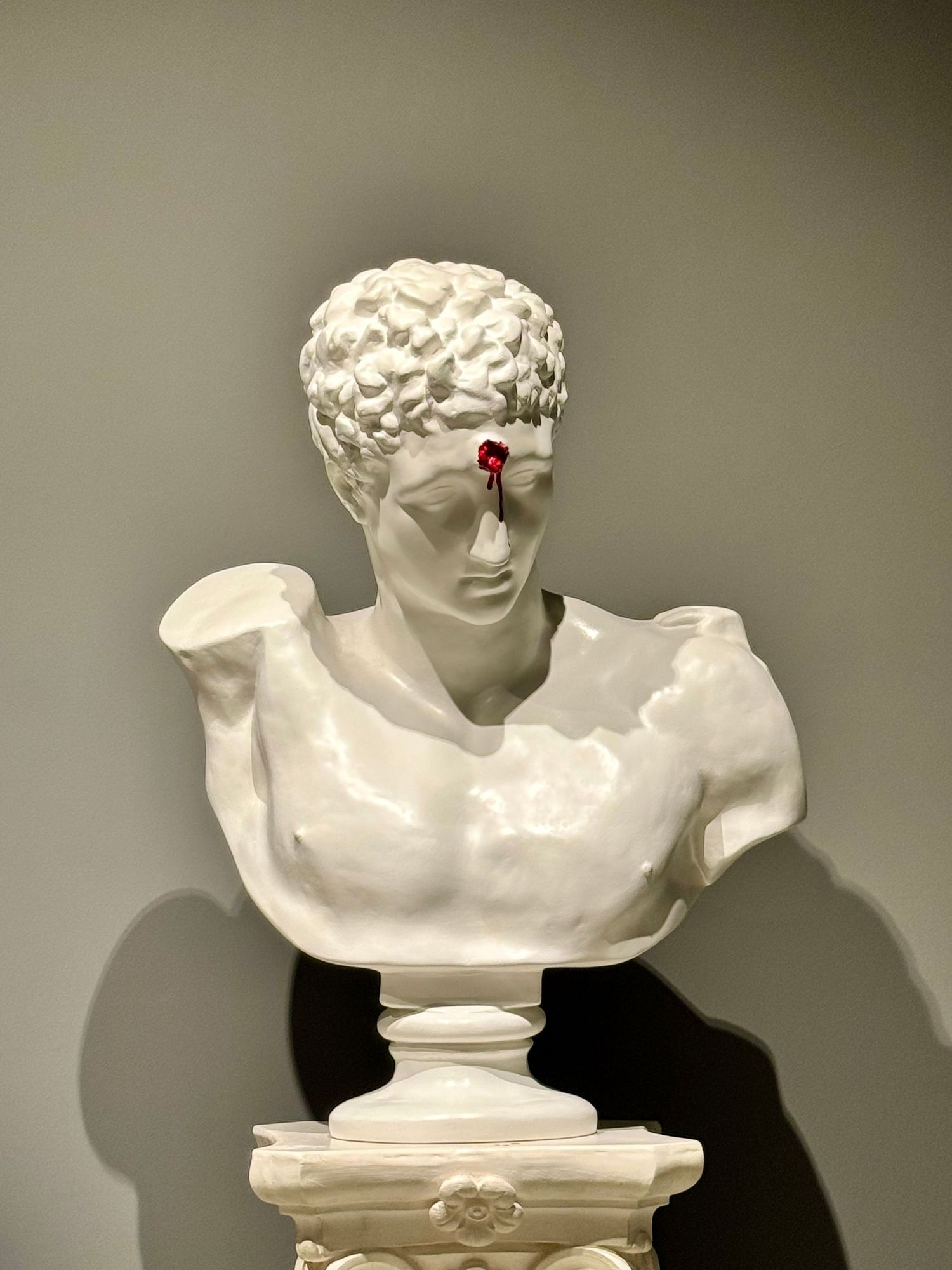 Classical white marble bust with red detail displayed on pedestal.