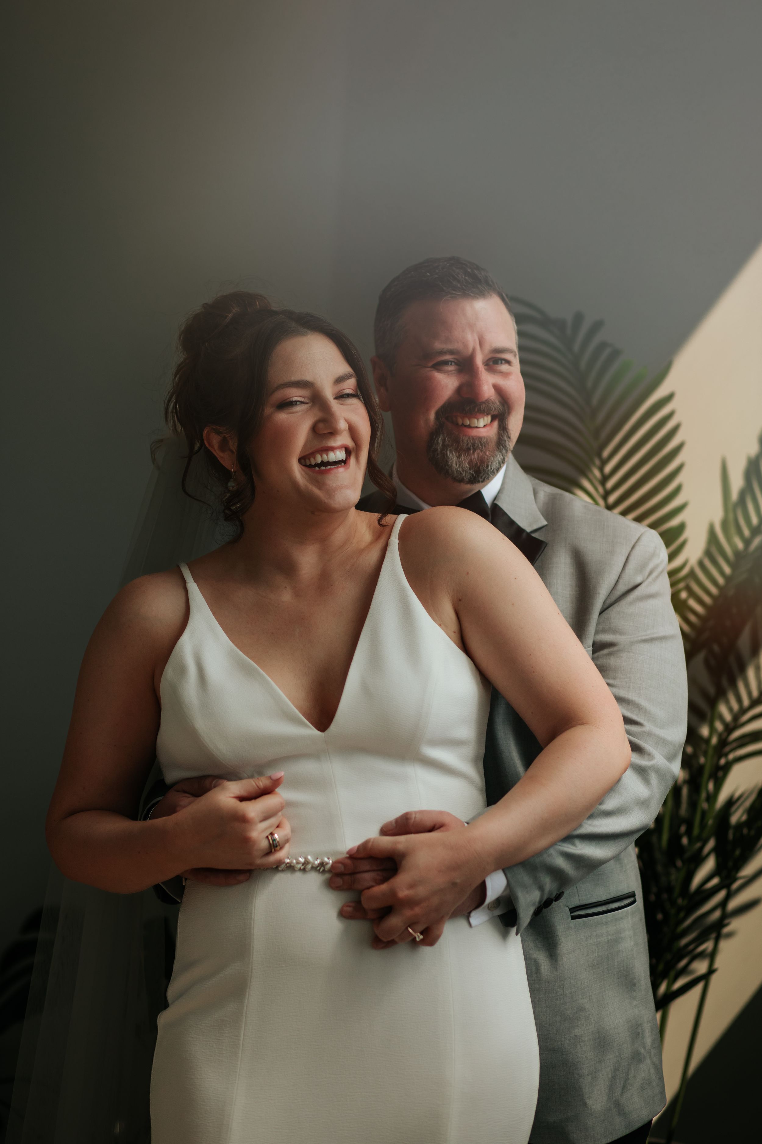 A couple shares joyful laughter during an intimate indoor photo session with palm leaves in the background in Indianapolis Indiana.