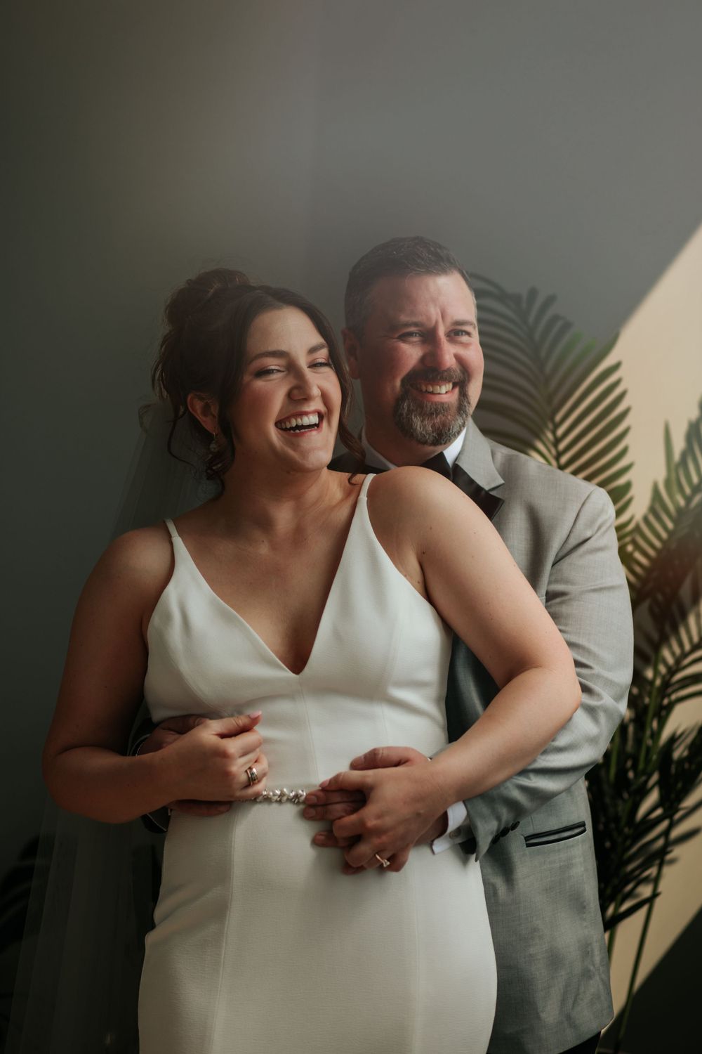 A couple shares joyful laughter during an intimate indoor photo session with palm leaves in the background in Indianapolis Indiana.