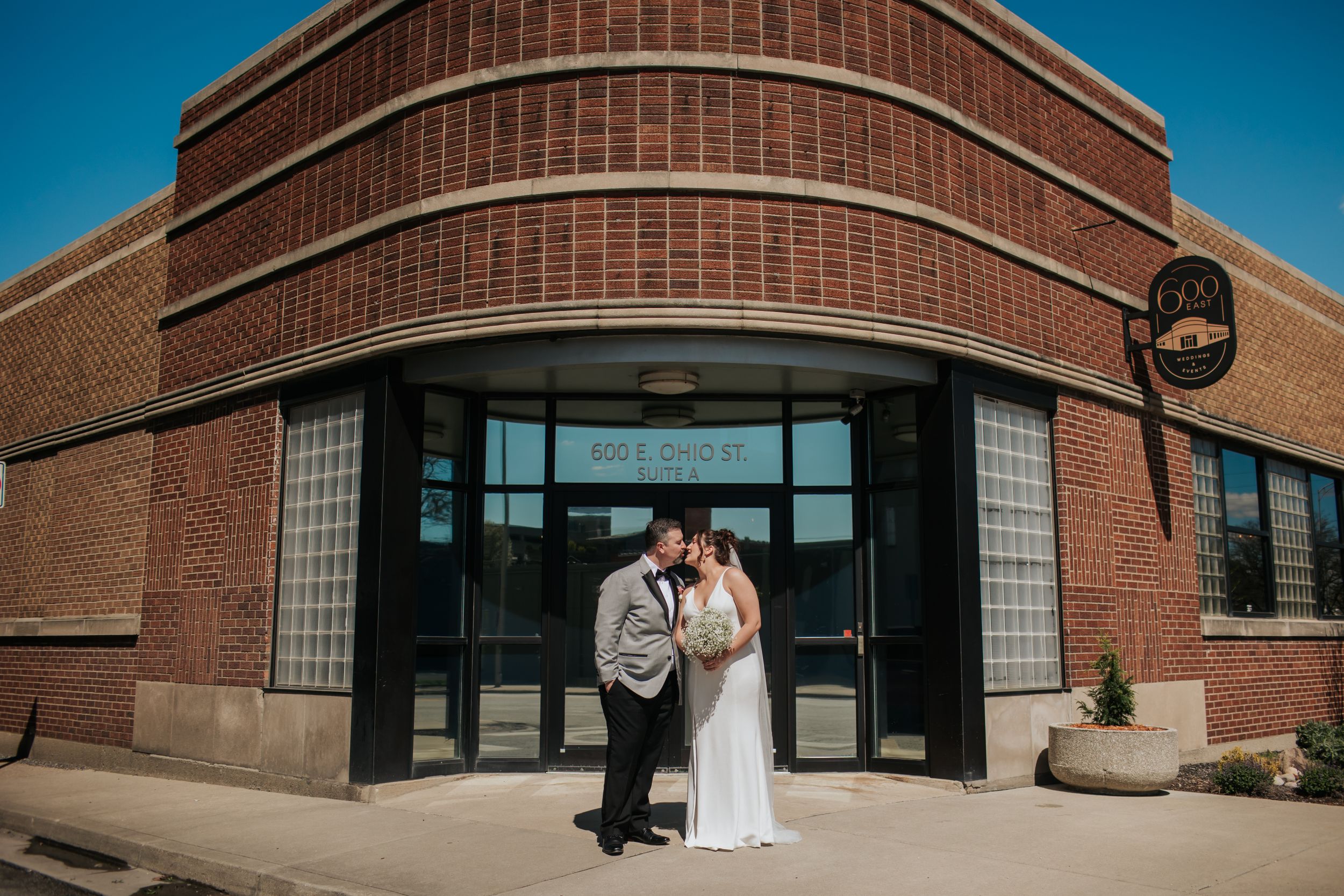 A wedding couple shares a romantic moment outside a modern brick building with large windows in Indianapolis Indiana.