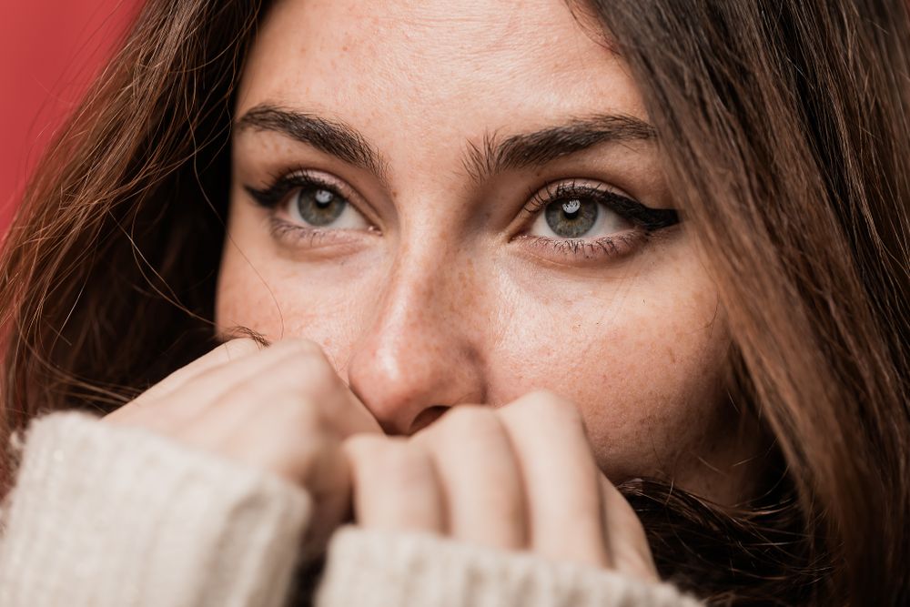 Close up shot of expressive eyes peering over hands covering lower part of the face.