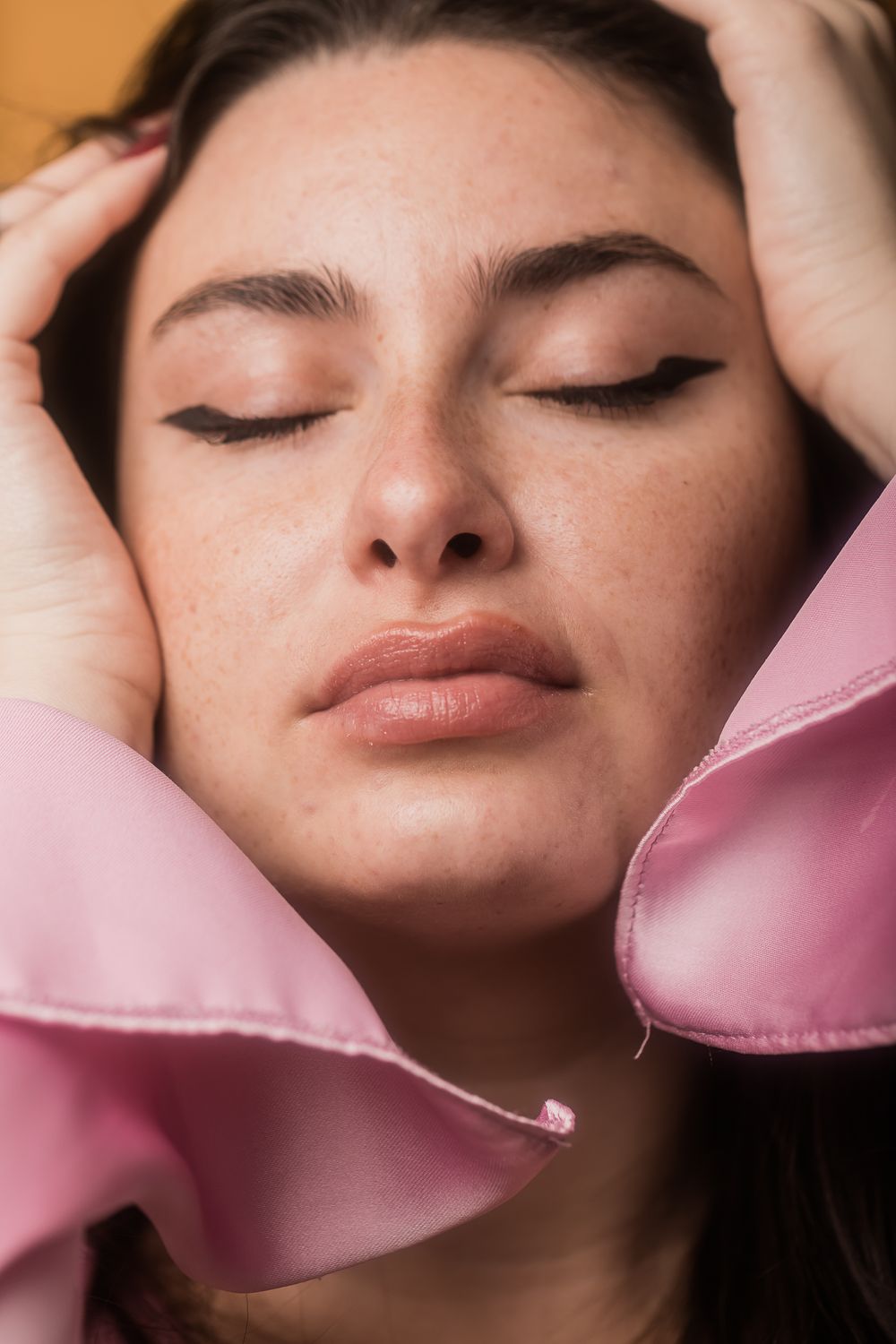 Close-up beauty portrait featuring pink silk and soft makeup with closed eyes and flawless complexion.