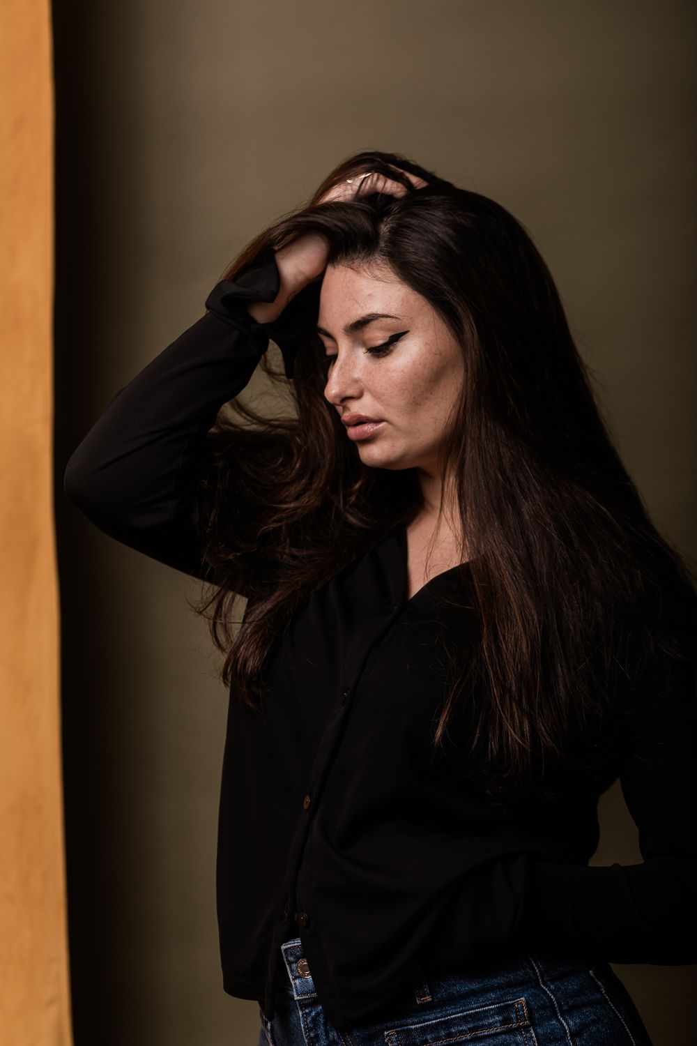 Atmospheric portrait of someone in black clothing against a warm toned wall with dramatic lighting.