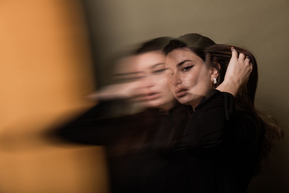 An artistic portrait with motion blur effect showing a person in black against an orange background.