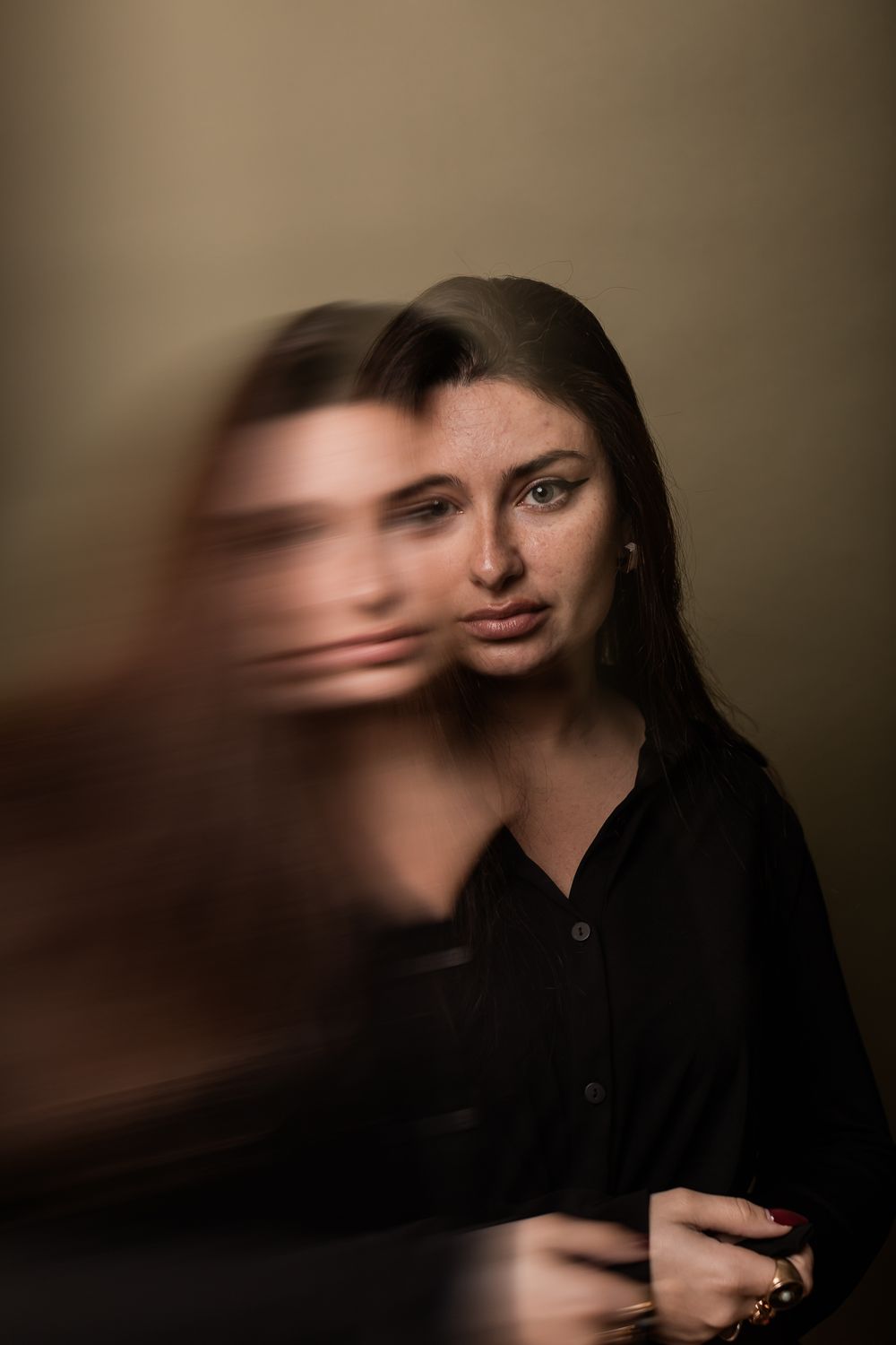 Artistic portrait with motion blur effect showing double exposure in dark moody lighting against brown background.