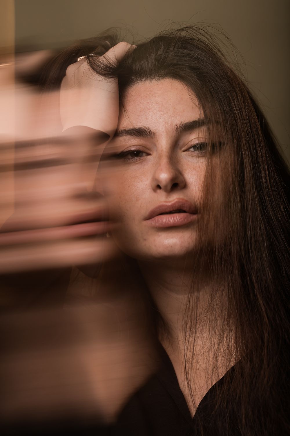 Artistic portrait with blurred motion effect showing long dark hair and natural makeup in warm brown tones.