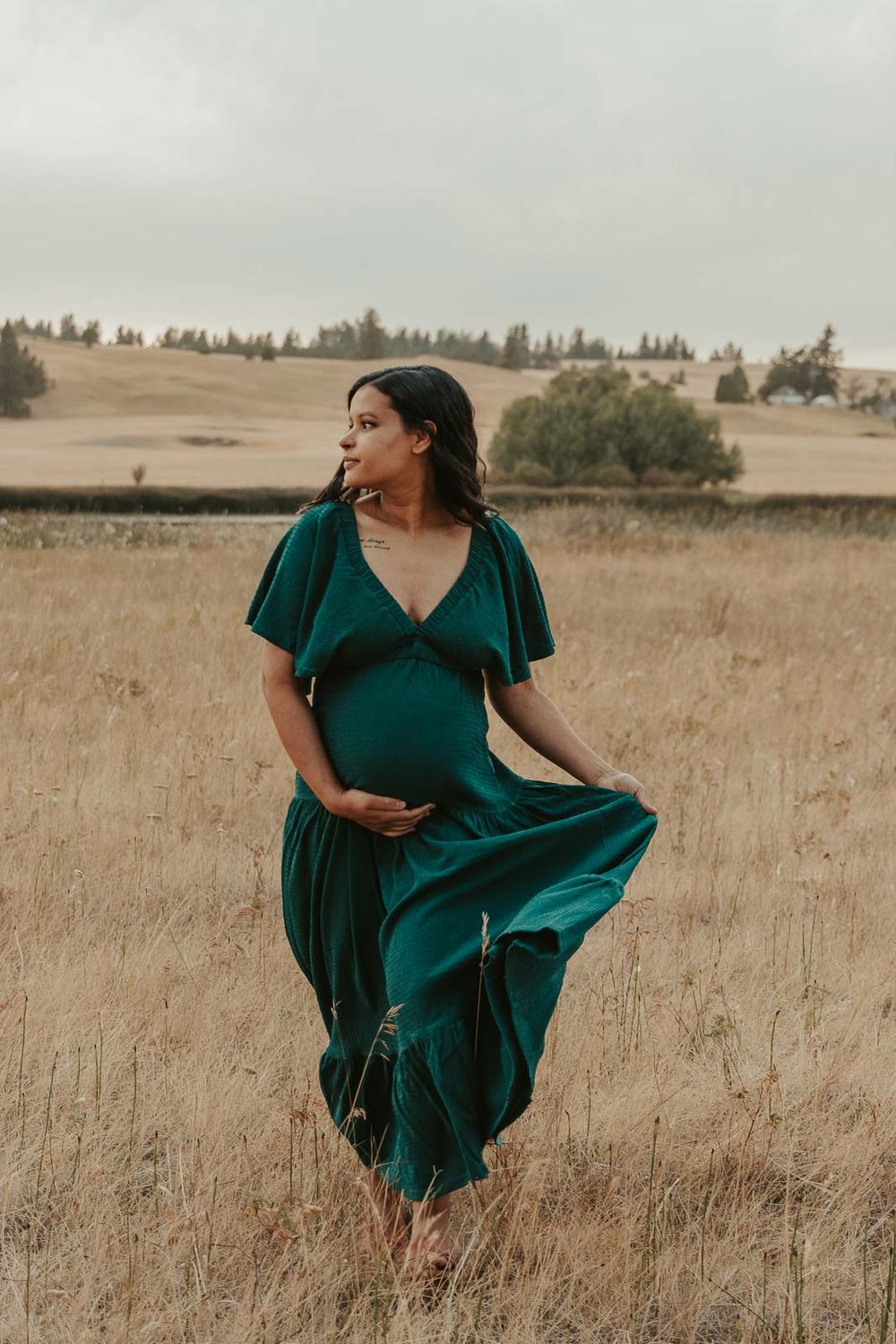 Pregnant mother in a flowing emerald green maternity dress standing in a golden field at The Point at Horseshoe Lake