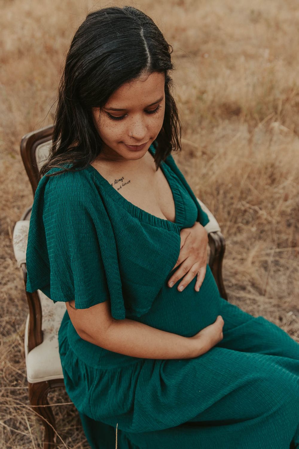 Pregnant mother in a flowing emerald green maternity dress standing in a golden field at The Point at Horseshoe Lake