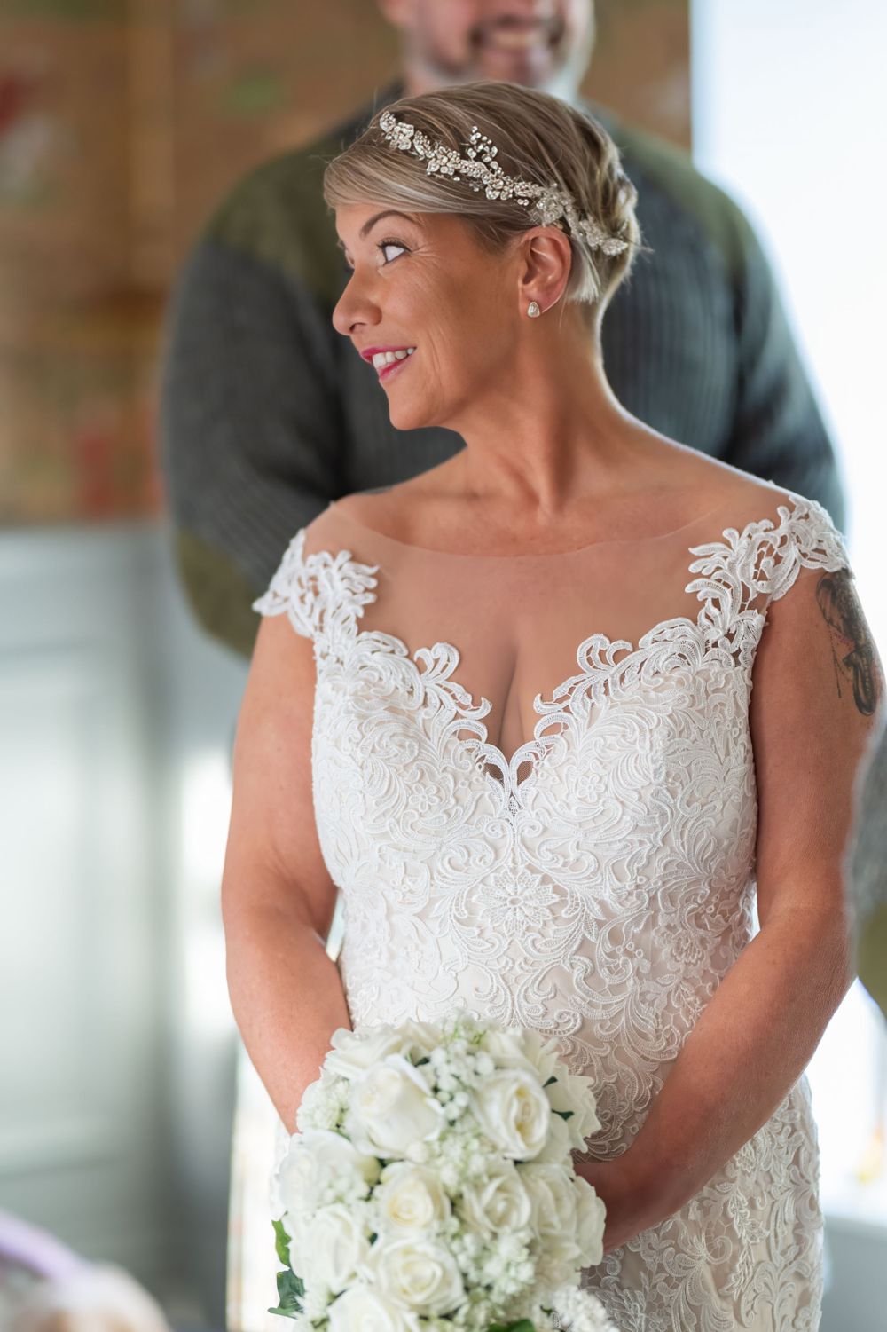 Bride holding white rose bouquet in detailed lace wedding gown with cap sleeves.