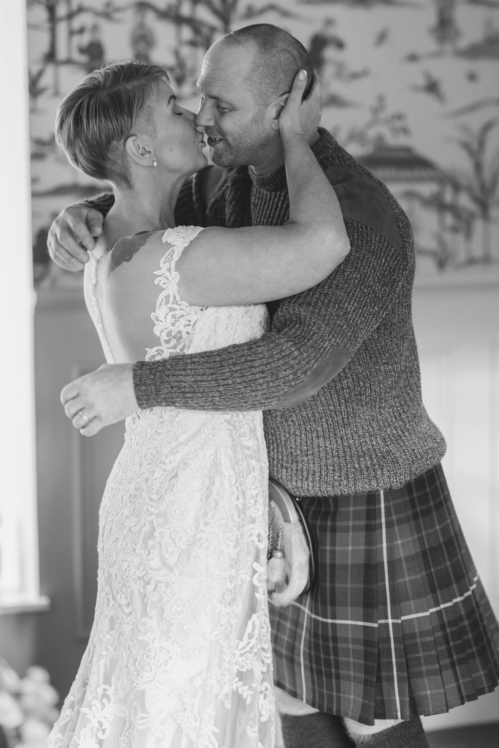 Black and white photo of newlyweds dancing, with the groom in a kilt and bride in lace dress.