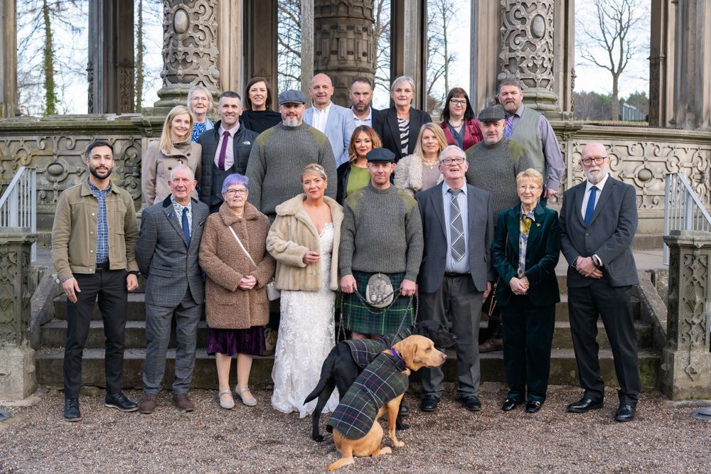 Large group wedding photo with guests lined up outside a stone building.