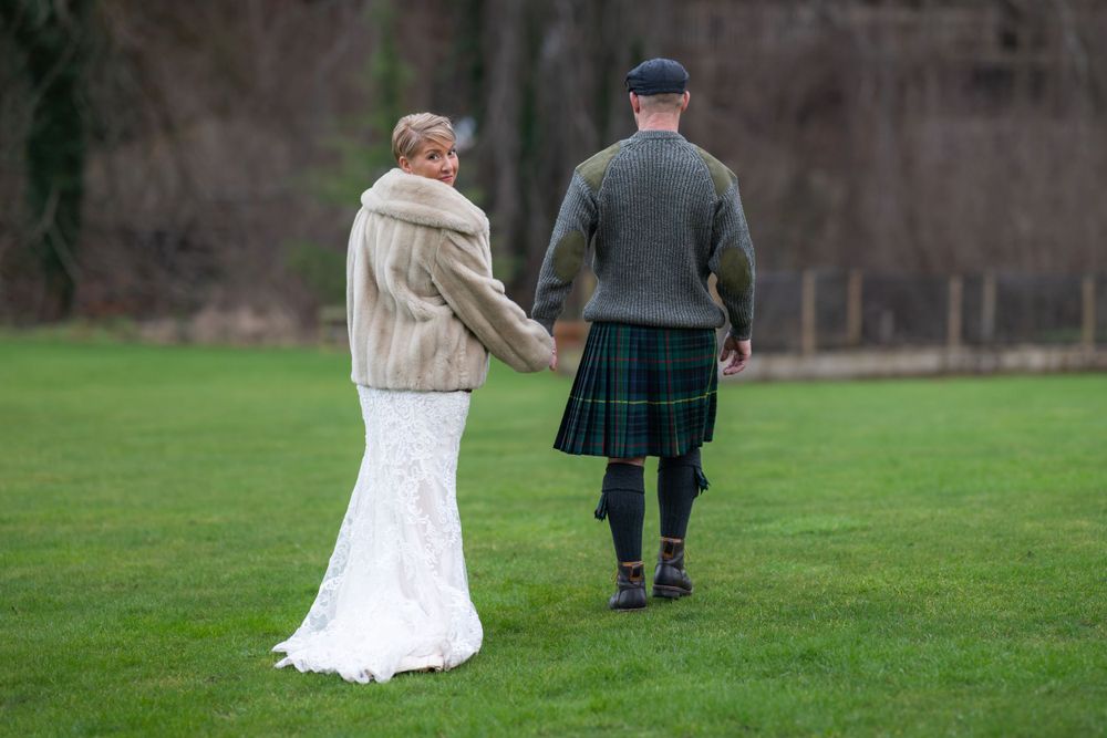 Couple walking across a green lawn during their Scottish wedding celebration.