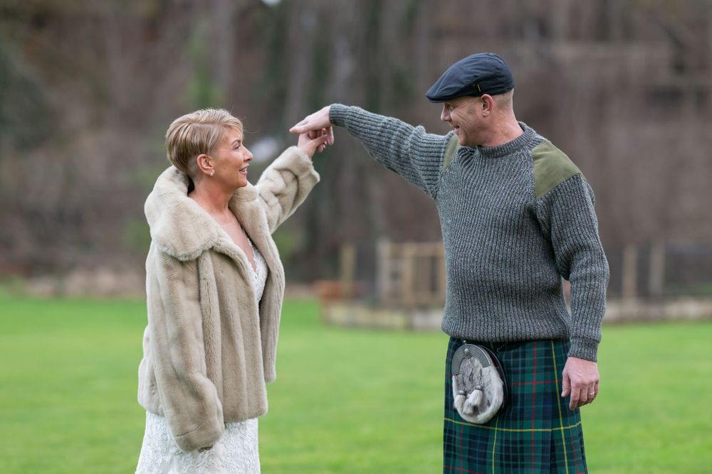 Newlyweds strolling through a garden with the groom in traditional Scottish attire.