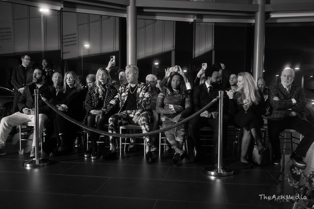 Black and white image of people seated in rows at a dimly lit indoor gathering.