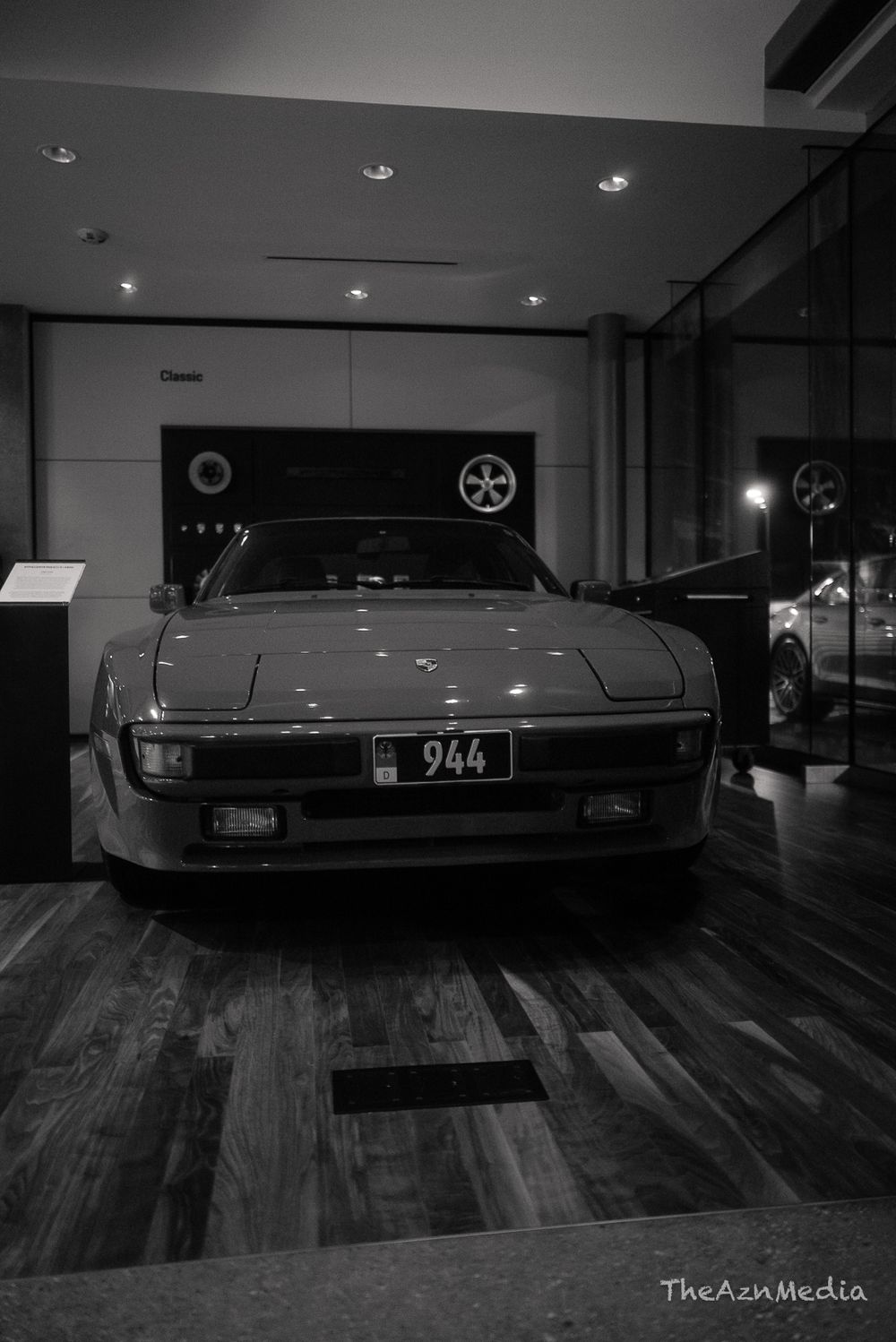 Classic Porsche sports car on display in a showroom with hardwood floors and spotlighting.