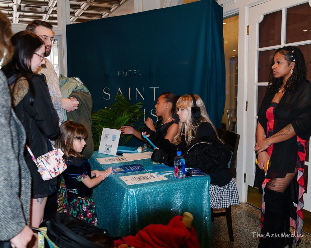 Event setup with teal tablecloth and Hotel Saint sign during meet and greet.