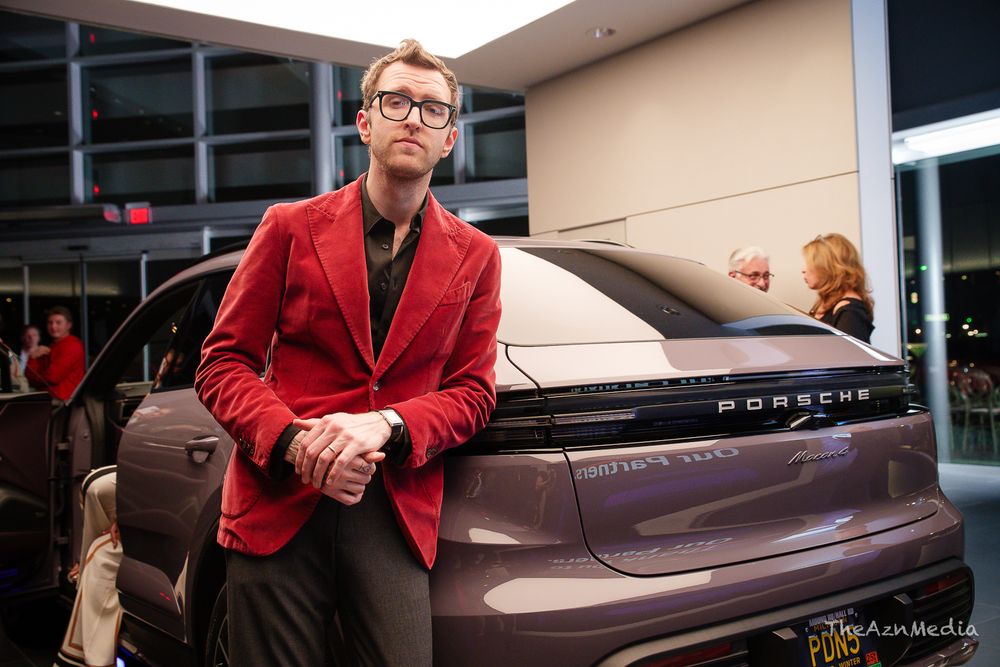 Person in bright red blazer standing next to a modern Porsche SUV.