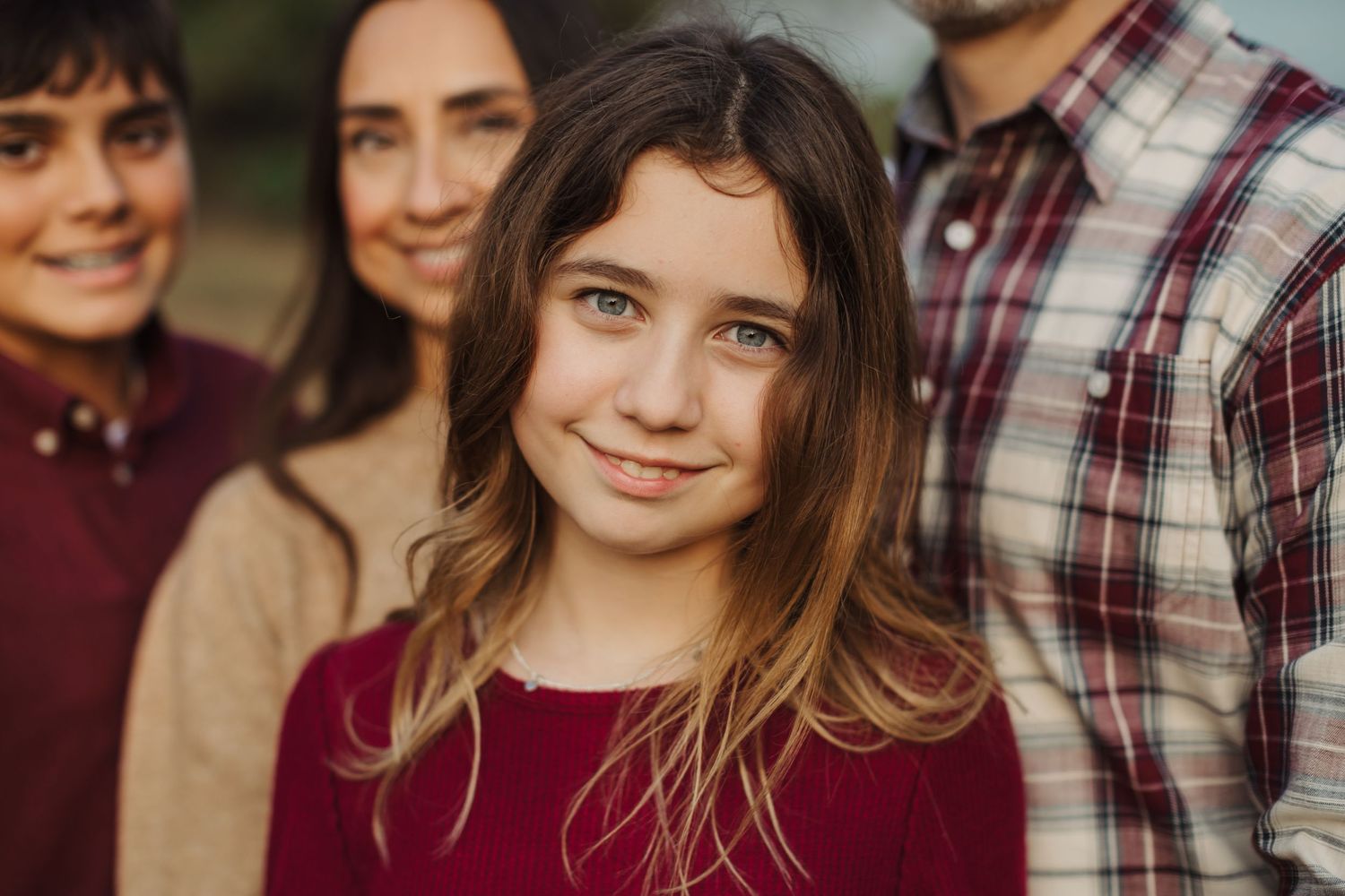Family group portrait in coordinating burgundy and plaid outfits outdoors.