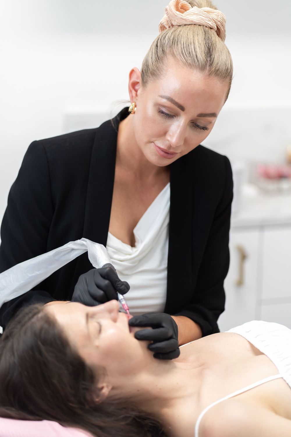 Professional esthetician performs a facial treatment on client lying on pink spa bed in modern salon.