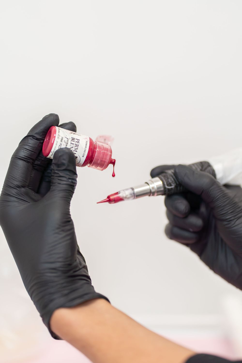 Black-gloved hands preparing pink cosmetic solution in medical syringe.
