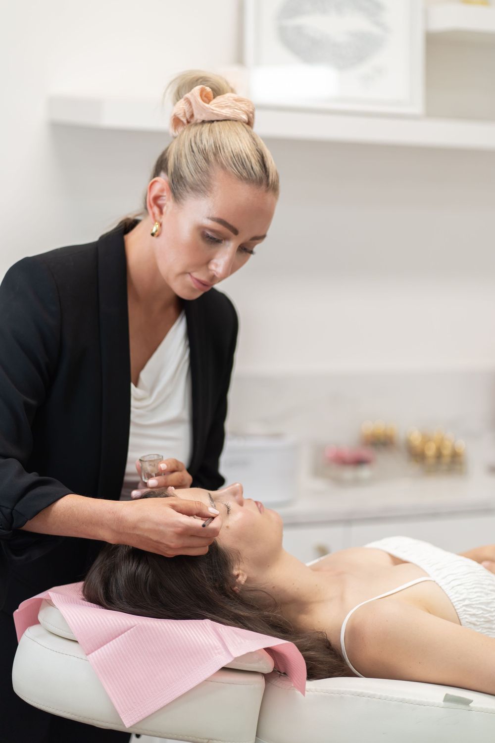 Skilled beautician provides facial massage treatment to client on pink treatment bed.