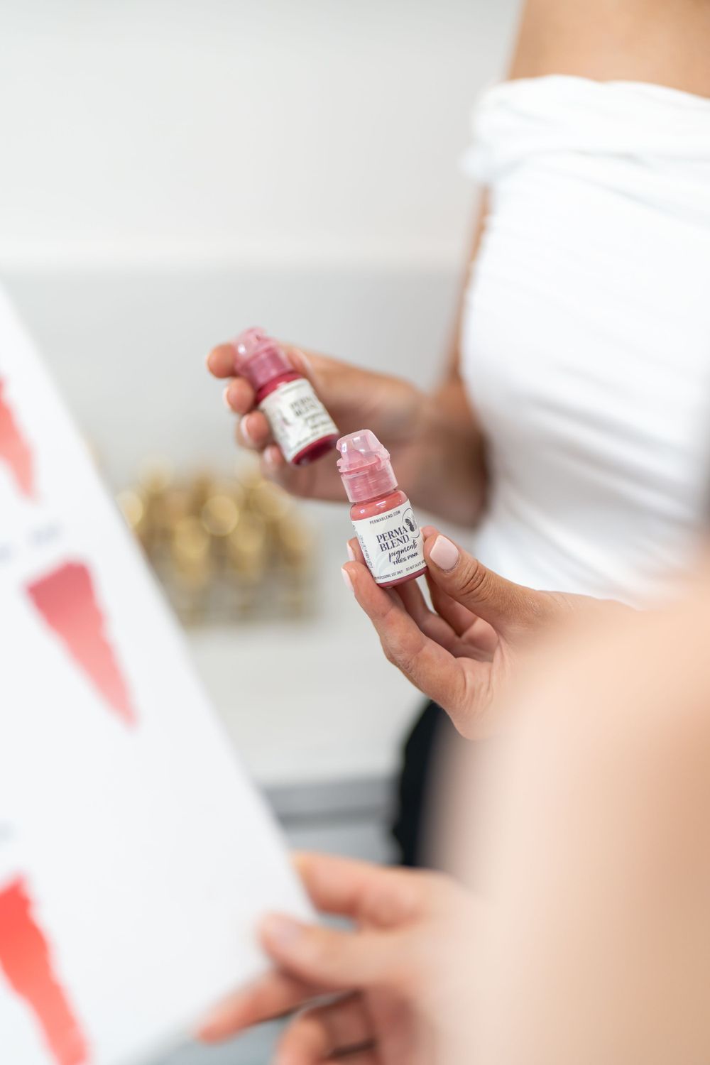 Hands holding small pink product bottles against white background.
