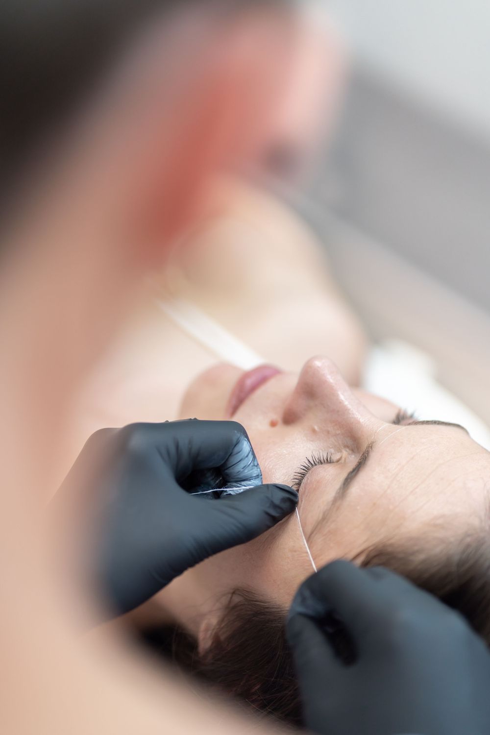 Close-up of professional eyebrow treatment being performed with black gloves.