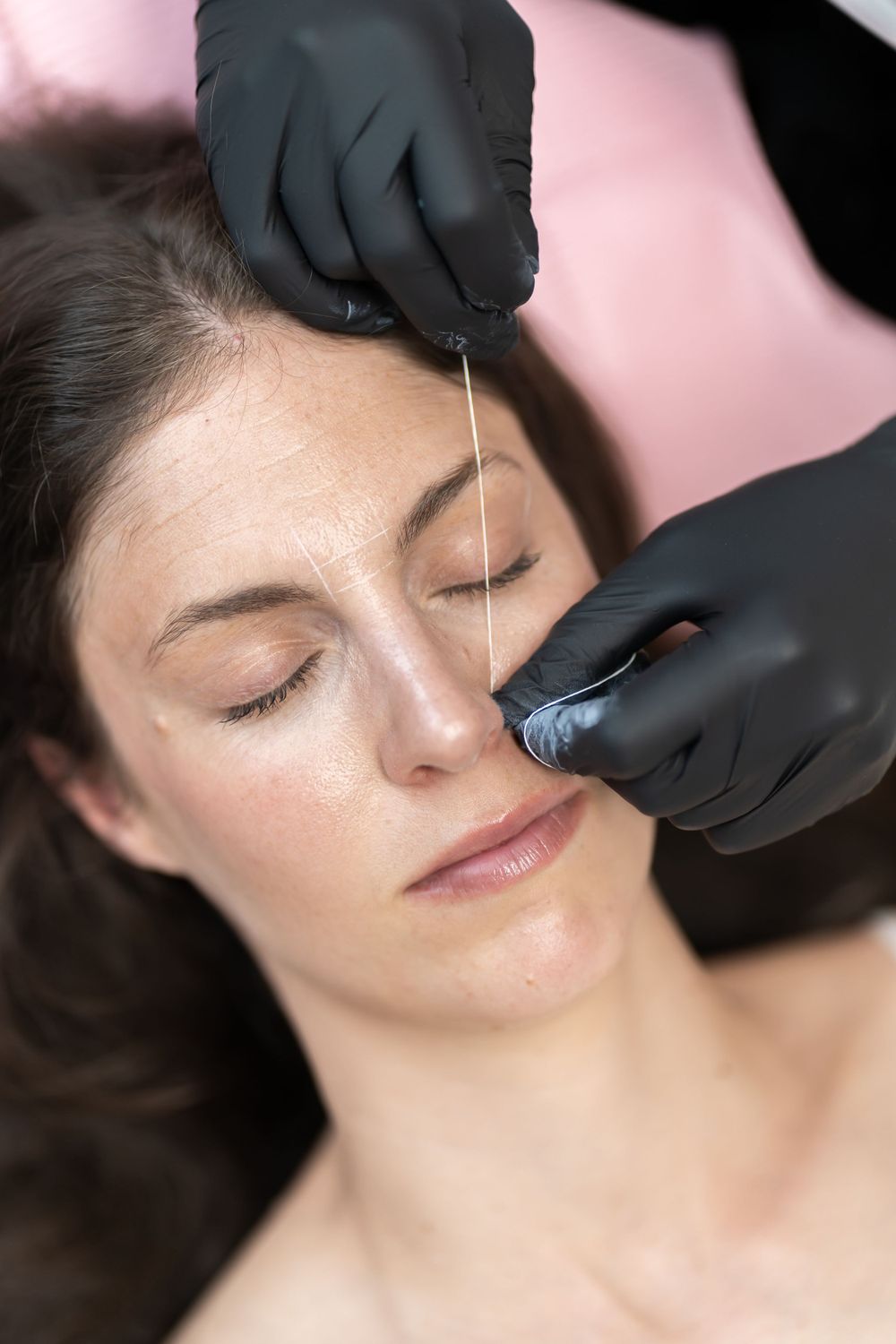 Detailed view of eyebrow threading procedure with black gloved hands.