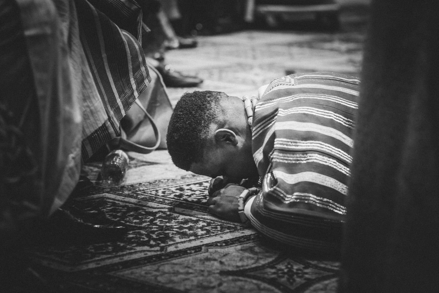 A tender black and white photograph showing someone asleep on a striped pillow on a patterned floor.
